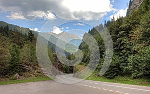 Beautiful mountain road landscape green forest trees winding alpine Alps Swiss Switzerland empty summer travel blue sky mountains