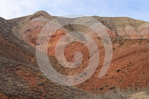 Beautiful mountainous terrain. Steppe landscape with dry grass, red mountains and blue sky. Horizontal photo