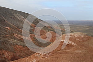 Beautiful mountainous terrain. Steppe landscape with dry grass, red mountains and blue sky. Horizontal photo