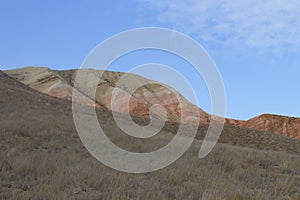Beautiful mountainous terrain. Steppe landscape with dry grass, red mountains and blue sky. View from a height, panorama.