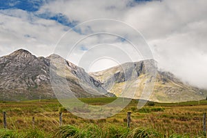 Beautiful mountains in Connemara, county Galway, Ireland; Warm sunny day, Clouds over peaks, Vast green fields