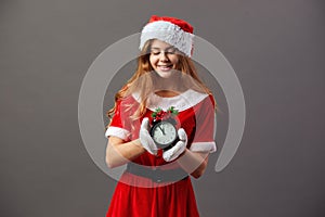 Beautiful mrs.Santa Claus dressed in the red robe, Santa`s hat and white gloves is holding a clock that shows five to