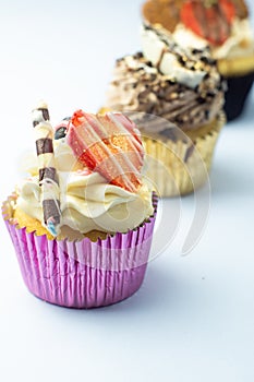 Beautiful muffin cupcakes decorated with fruits, chocolate, golden sprinkles and cookies, in one line. Many pastries on light back