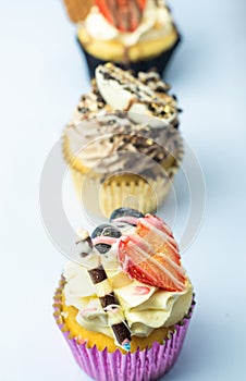 Beautiful muffin cupcakes decorated with fruits, chocolate, golden sprinkles and cookies, in one line. Many pastries on light back