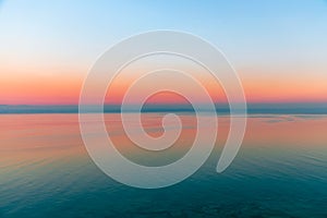 Beautiful multicolor sunset reflected in the waters of Lake Garda, Italy. Skyline. Visible coastline in the evening fog. Winter photo