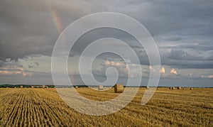 Beautiful multicolored rainbow over a sloping wheat field with large rolls of straw