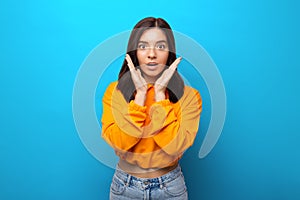 Beautiful multiethnicity woman in orange trendy shirt happily surprised expression against blue background