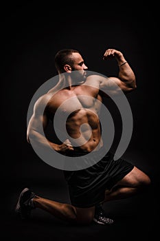 A beautiful, muscular man on a black background. A bodybuilder is posing in a studio. Sports concept.