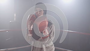 Beautiful muslim female boxer in hijab fighting live camera in slowmo. Portrait of young woman training on boxing ring
