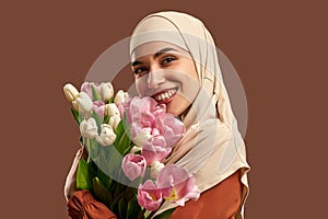 Beautiful Muslim woman in a beige hijab holding a bouquet of white and pink tulips smiling and looking at the camera. Beauty,