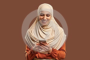 Beautiful Muslim woman in a beige hijab holds a phone in her hands and smiles. Advertising, technology, devices