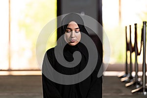 Beautiful Muslim woman in a black dress with hijab praying in a mosque.