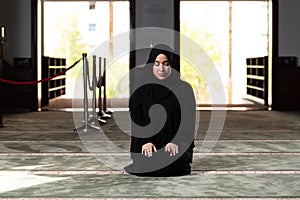 Beautiful Muslim woman in a black dress with hijab praying in a mosque.