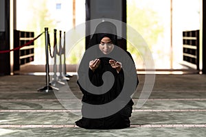 Beautiful Muslim woman in a black dress with hijab praying in a mosque.