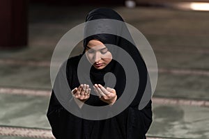 Beautiful Muslim woman in a black dress with hijab praying in a mosque.