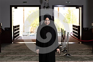 Beautiful Muslim woman in a black dress with hijab praying in a mosque.