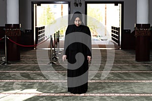 Beautiful Muslim woman in a black dress with hijab praying in a mosque.