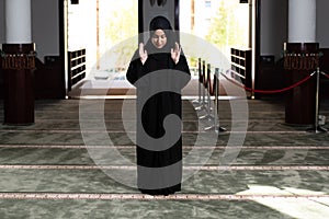 Beautiful Muslim woman in a black dress with hijab praying in a mosque.