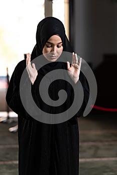 Beautiful Muslim woman in a black dress with hijab praying in a mosque.