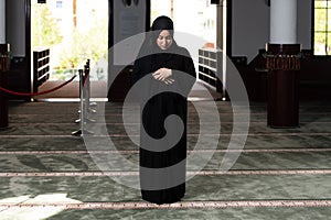 Beautiful Muslim woman in a black dress with hijab praying in a mosque.