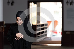 Beautiful Muslim woman in a black dress with hijab praying in a mosque.