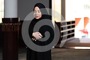 Beautiful Muslim woman in a black dress with hijab praying in a mosque.