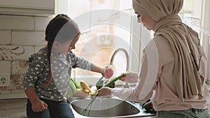 Beautiful muslim woman with her four year old daughter is washing vegetables in the kitchen sink
