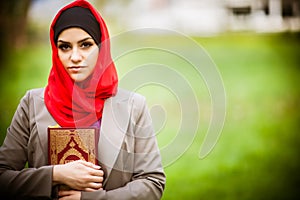 Beautiful muslim woman wearing hijab and holding a holy book Koran.