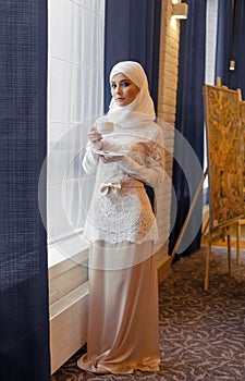 Beautiful Muslim woman in a white wedding dress standing at window photo