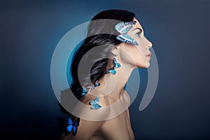 Beautiful mysterious woman with butterflies blue color on her face, brunette and paper artificial blue butterflies on the girls