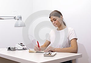 Beautiful nail beautician makes notes in notebook with pen, sitting at workstation photo