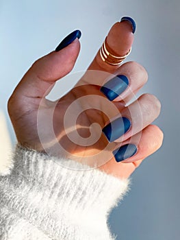 Beautiful nails manicure photo. Dark blue color matte top nail polish. Female hand, rings, closeup photo, aesthetics