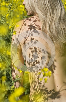 Beautiful naked blonde woman among yellow flowers