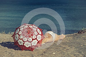 Beautiful naked female lies on the beach under a red umbrella. Girl on the sand under the umbrella