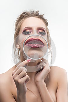Beautiful naked shoulders girl shows an enlarged with a magnifying glass her lips.