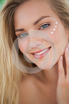 Beautiful natural blonde smiling at camera with eye cream on