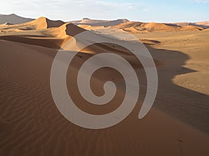 Beautiful natural curved ridge line and wind blow pattern of rusty red sand dune with soft shadow on vast desert landscape