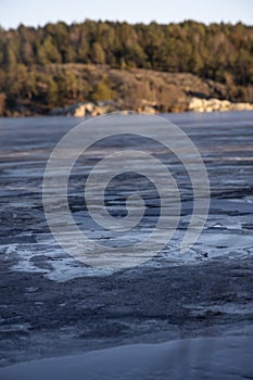 Beautiful natural Scandinavian landscape. Frozen lake with forest and stones at the shore line. Sunny late autumn or winter day in