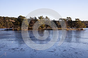 Beautiful natural Scandinavian landscape. Frozen lake with forest and stones at the shore line. Sunny late autumn or winter day in