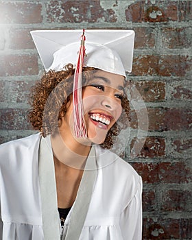 Beautiful Natural smiling mixed race girl in white cap and gown with red and white tassels photo