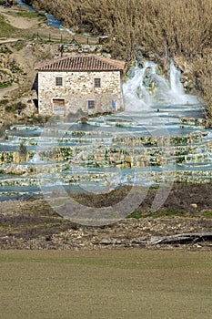 The beautiful natural thermal springs of Saturnia Cascate del Mulino, Grosseto, Tuscany, Italy, next to a typical stone cottage photo