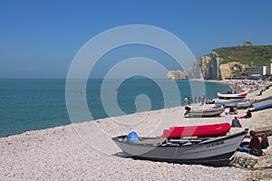 Beautiful nature landscape photo of resting people in pebble beach at Etretat. Colorful wooden fishing boats on the shore.