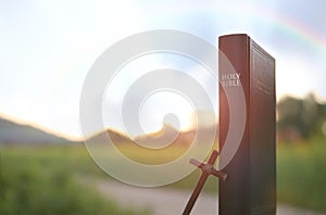 Beautiful nature landscape with rainbow, bible book and cross of Jesus