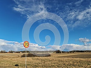 Beautiful nature landscape view on sunny spring day. Speed limit sign  on yellow field and blue sky with white clouds background