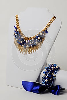 Beautiful navy blue necklace, gold chain and bracelet with big satin ribbon on a mannequin in front of white background