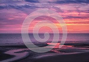 Beautiful near dark twilight over a calm flat sea with purple sky and blue clouds reflected in water on the beach