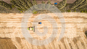 A beautiful new combine harvester dumps grain into a truck trailer on the field. Aerial view