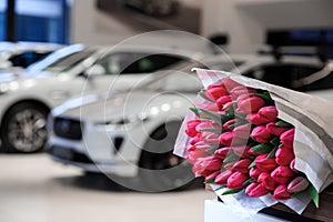 A beautiful new white car awaits its buyer in the cabin. colorful dark pink tulips