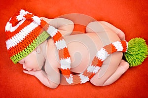 Beautiful newborn baby boy with cute cap sleeping peacefully on the soft red blanket