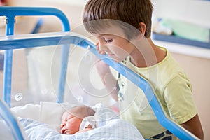 Beautiful newborn baby boy, laying in crib in prenatal hospital, his brothers looking at him